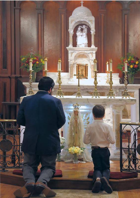 A father and son kneel in prayer before a statue of Our Lady of Fatima after a High Mass offered by Father Roger Arnsparger, pastor, at St. John the Baptist Church in Tryon. Photo by Giuliana Polinari Riley, Catholic News Herald