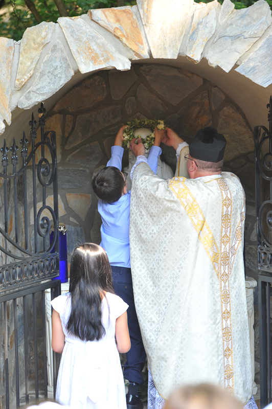 CHARLOTTE — Led by Father Christopher Roux, rector, children participated in a procession after Mass and crowned a statue of Mary at the Marian grotto outside St. Patrick Cathedral earlier this month. (Photo provided by Markus Kuncoro)