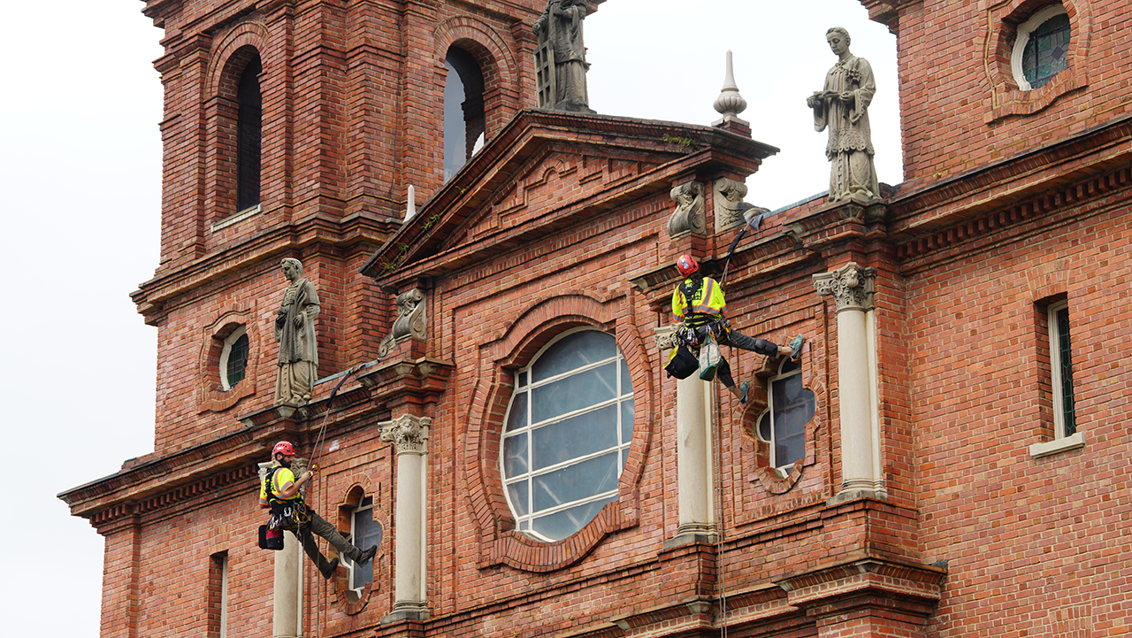 Technicians rappel down the front of St. Lawrence Basilica Oct. 10 to begin surveying the building’s exterior.