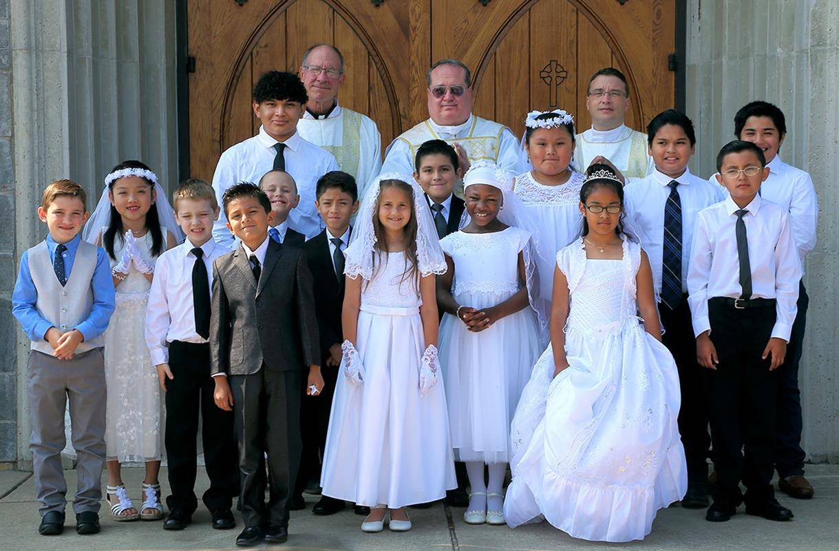 Also on May 19, 16 children received the sacrament of first Holy Communion during a Mass offered in English at Immaculate Conception Church. They are pictured with (from left) Deacon Steve Puscas, Father Burke and Deacon David Faunce.
