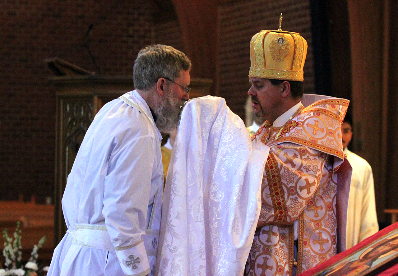 Newly-ordained Father Kevin kisses the phelonion, the Eastern version of a chasuble, as he is vested by the bishop.