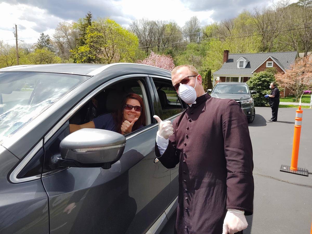 Father Casey Coleman at St. Mary Mother of God Church in Sylva said hello to parishioners as he and volunteers passed out blessed palm branches and bottles of holy water during a ‘“drive-through” procession in the church’s parking lot. (Della Sue Bryson)