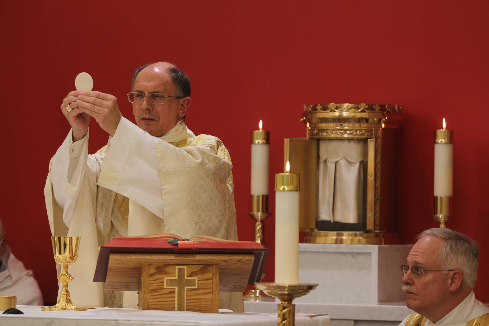 During the dedication Mass in the new chapel at Holy Family Church, Bishop Peter Jugish olds the Eucharist aloft as Deacon John Harrison looks on.