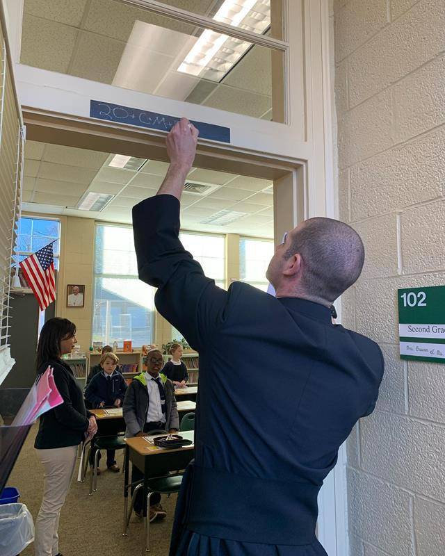 Father Christopher Gober and Father Darrwn Balkey lead St. Leo School in the Blessing of Dwellings Prayer. They then marked each door head with the prayer.