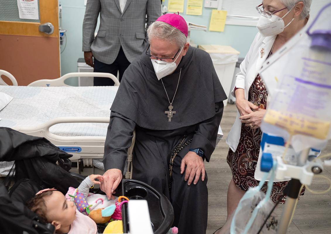 Charlotte Bishop-Elect Michael Martin, OFM Conv., greets Holy Angels' youngest resident during an April 9 visit. Belmont-based Holy Angels cares for children and adults with intellectual developmental disabilities and delicate medical conditions.