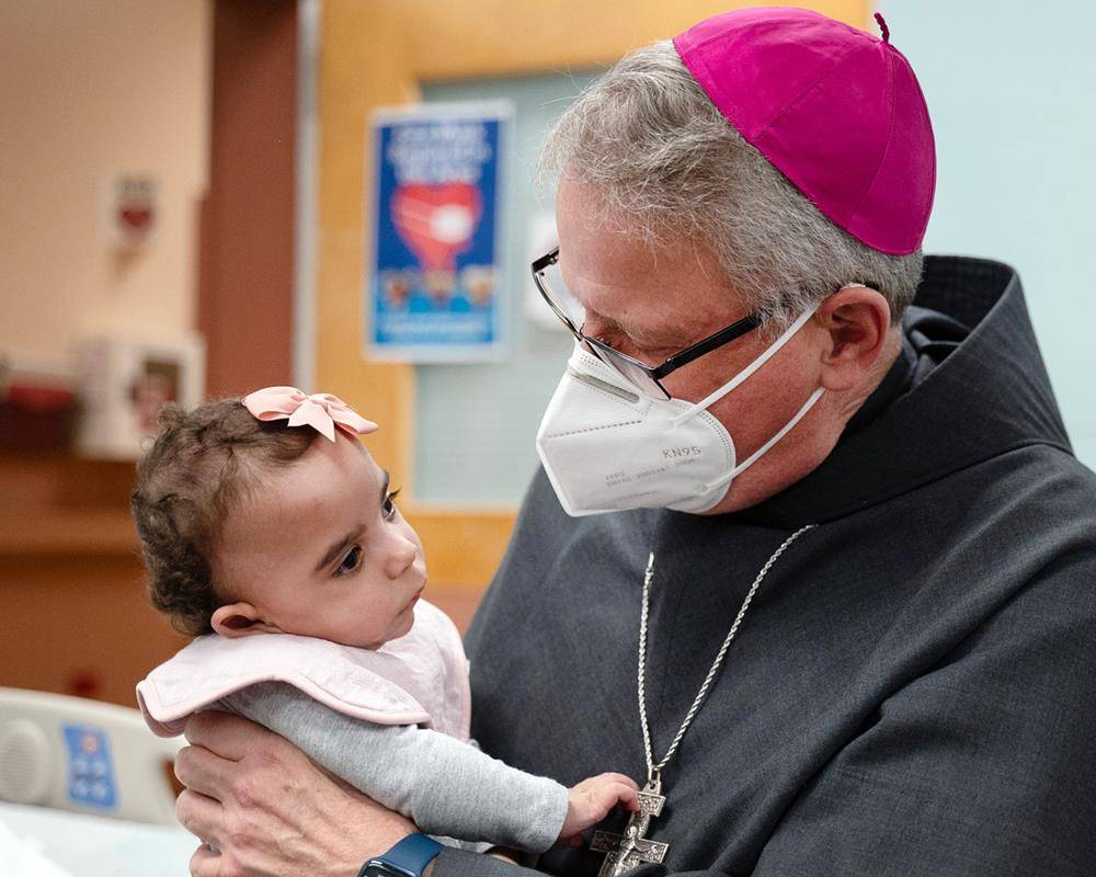 Bishop-Elect Michael Martin, OFM Conv., holds Holy Angels' youngest resident during his visit April 9 to the Diocese of Charlotte, following the Vatican's announcement that he will succeed retiring Bishop Peter Jugis.