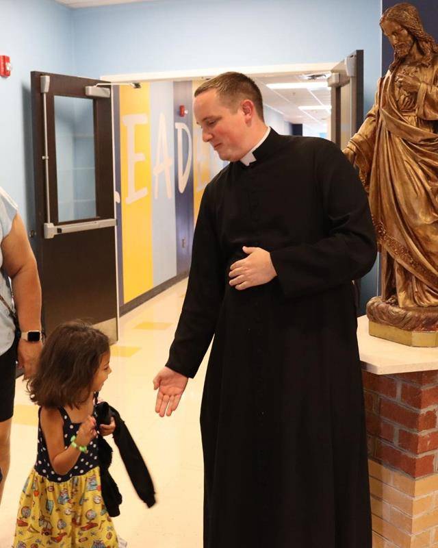Father Matthew Dimock high-fives a youngster in the halls of Sacred Heart School.